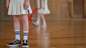 Close-up of a teen's legs in a gym, wearing sneakers and socks, with a blurred background.